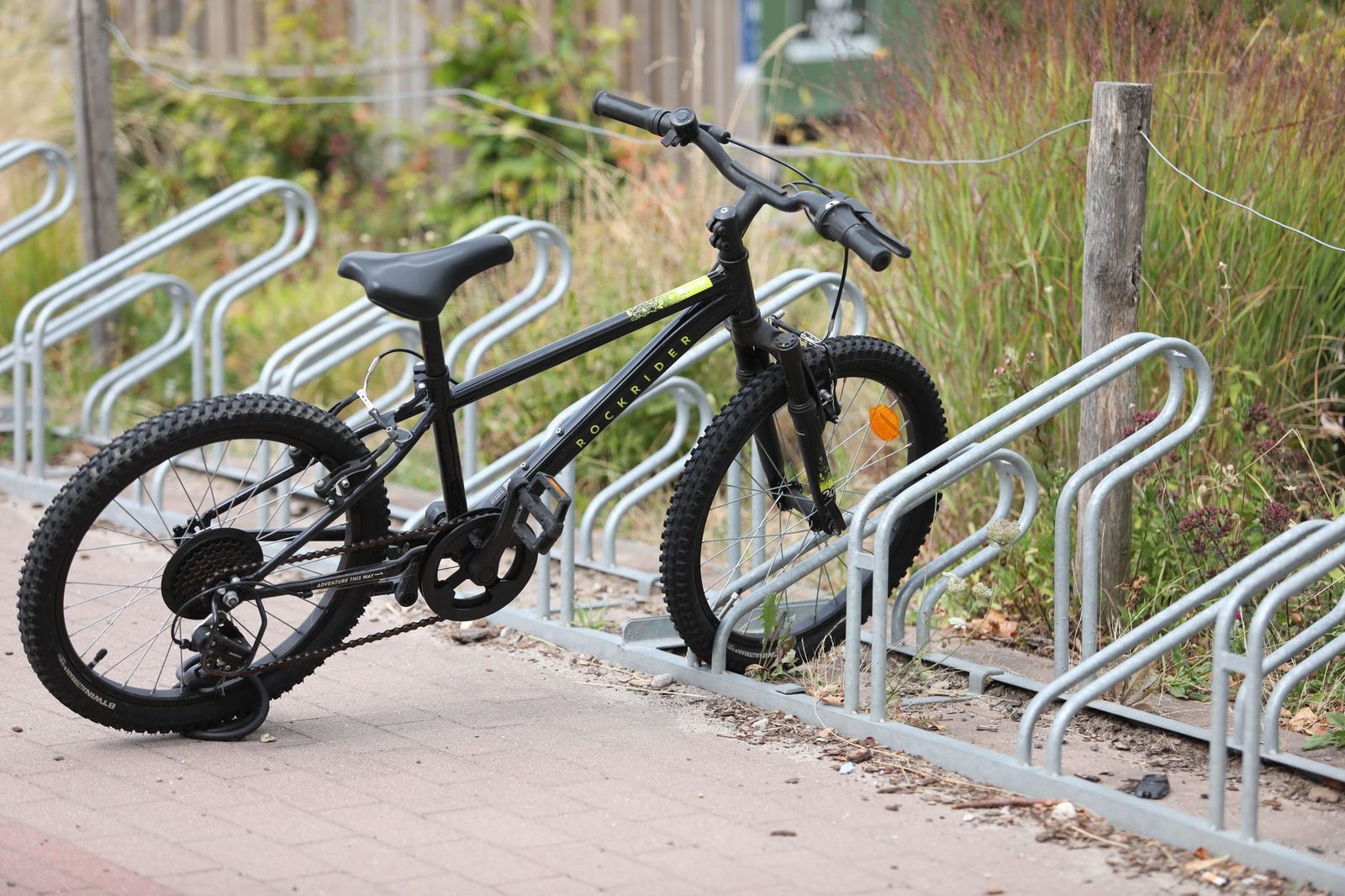 A child's bicycle locked to a metal bike rack on an outdoor walkway.