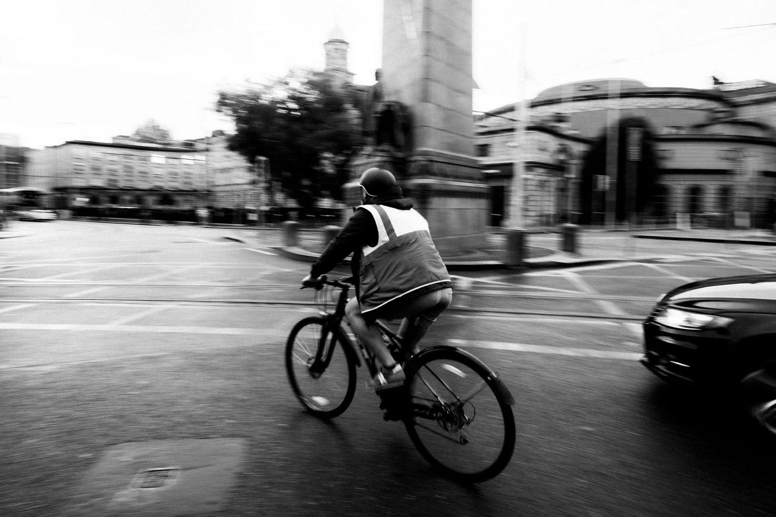 A cyclist rides along a busy city street in Dublin, Ireland, with pedestrians and traffic nearby.