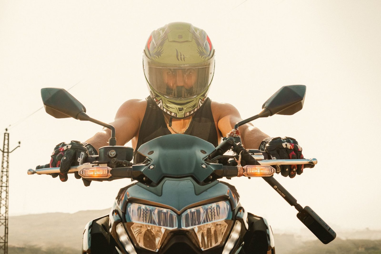 A man wearing a helmet rides a motorcycle toward the camera at sunrise.