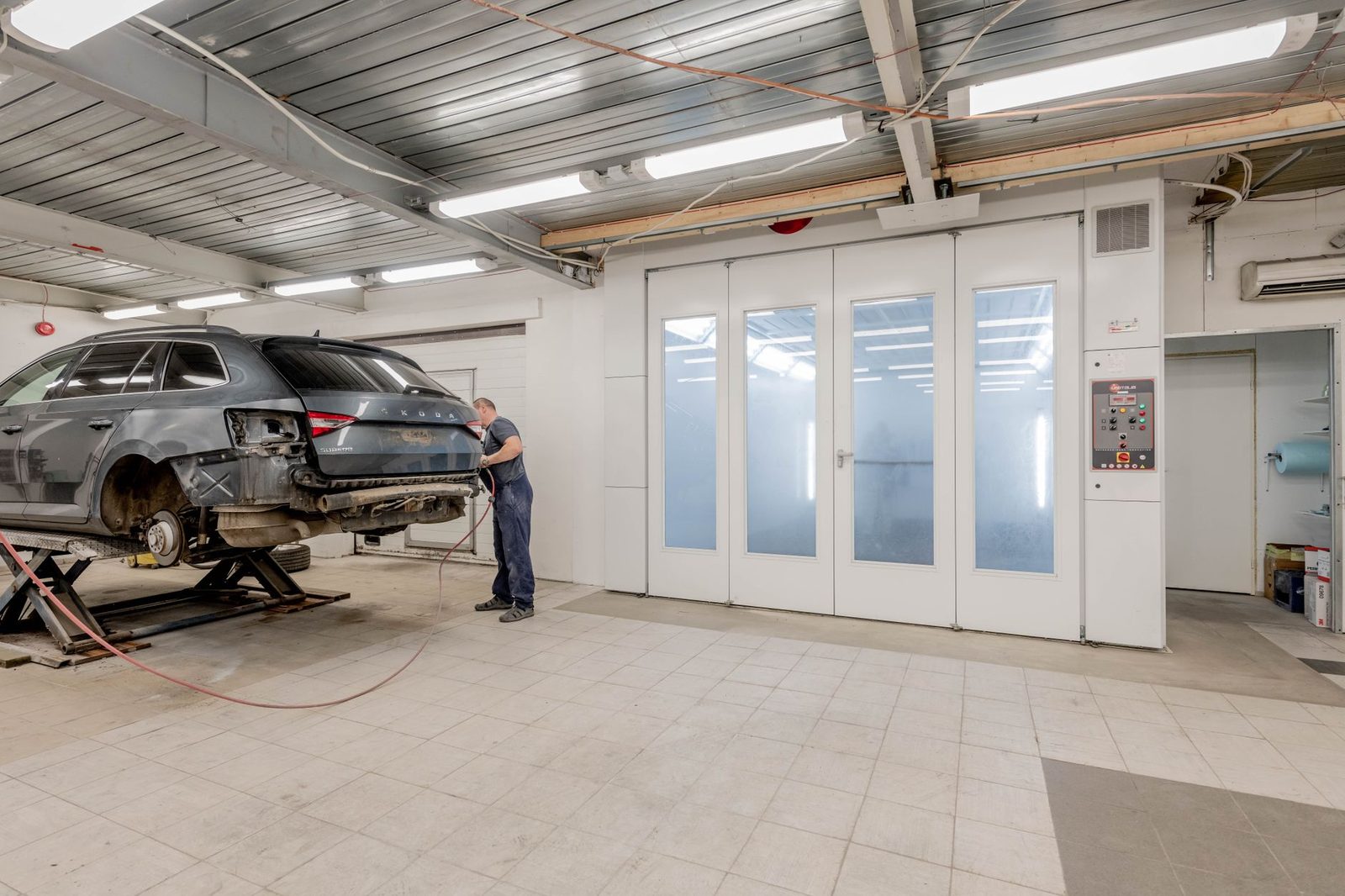 A mechanic works on a car engine inside a busy auto repair shop.