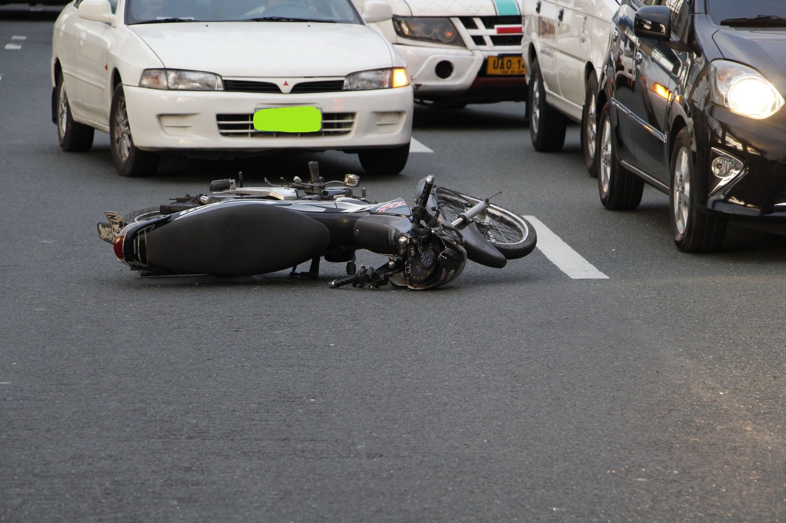 A motorcycle lying on its side on a city road with cars passing nearby