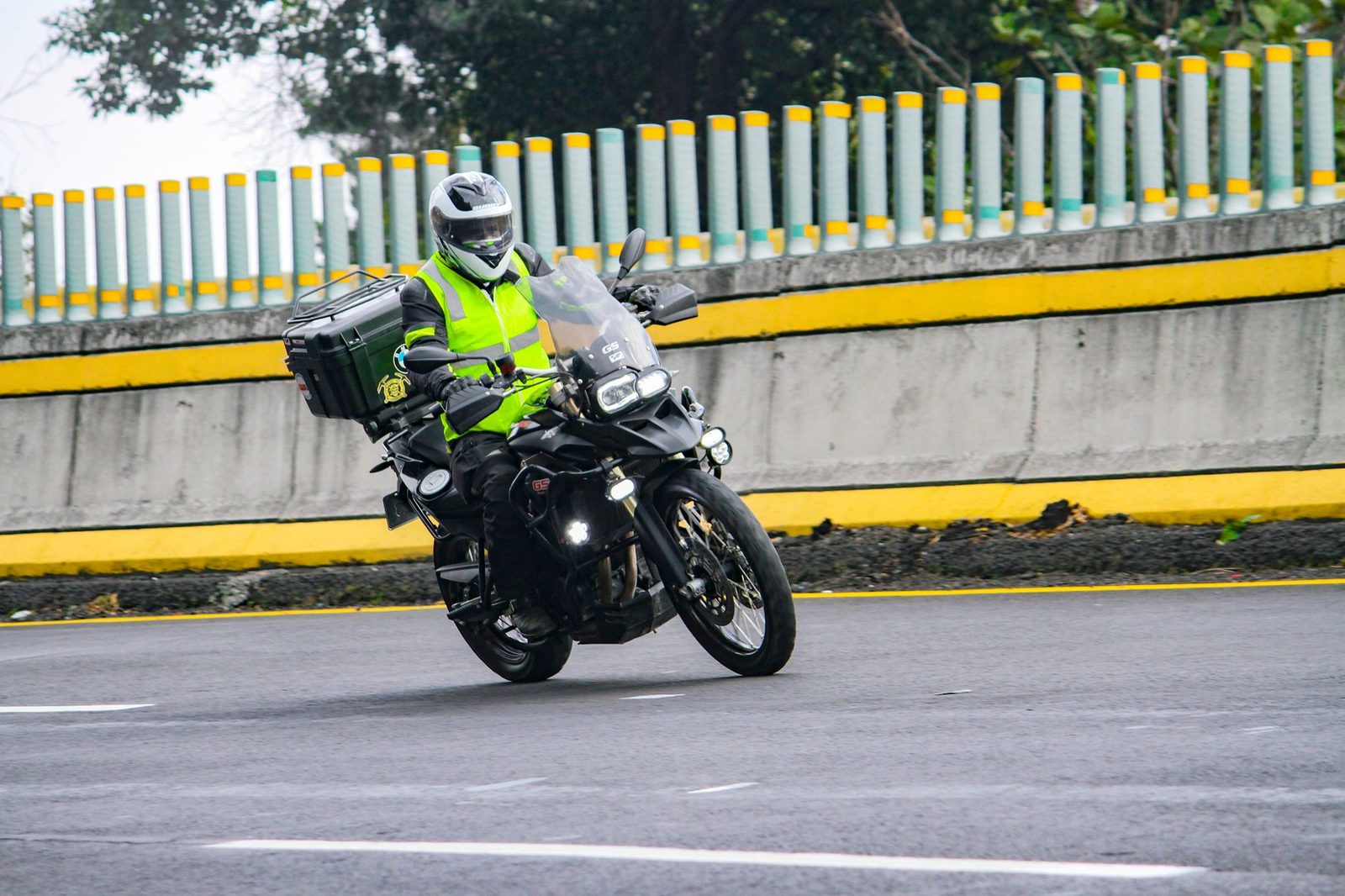 A motorcyclist in a high-visibility vest and safety gear rides through a curve on a road.