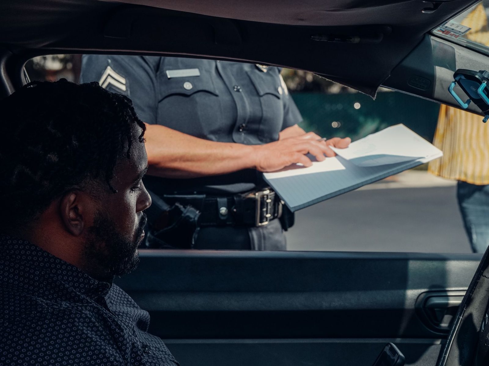 A police officer hands a traffic ticket to a driver through the car window.