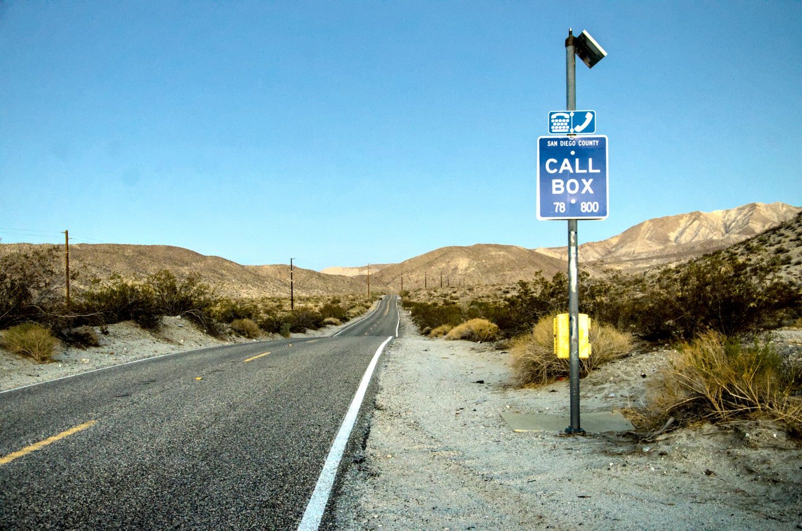 A quiet desert highway in California with a blue call box beneath a clear sky.