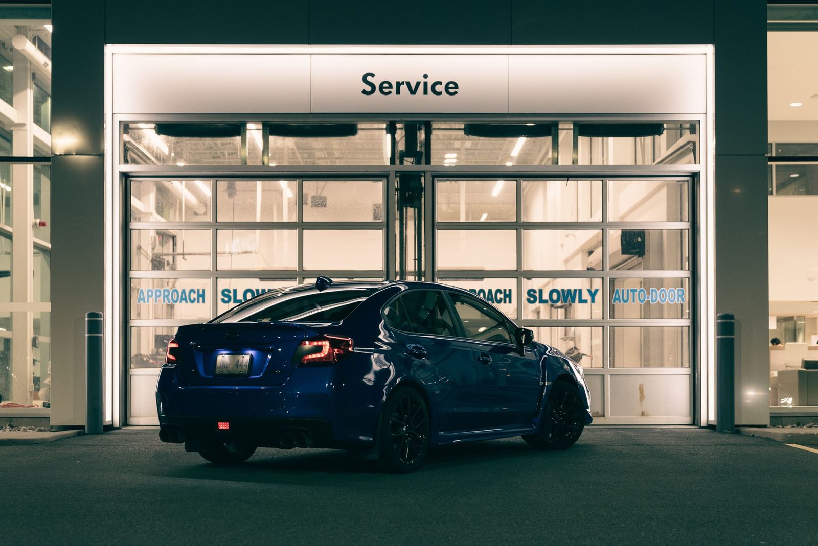 A sleek blue car parked at a brightly lit service station entrance at night.