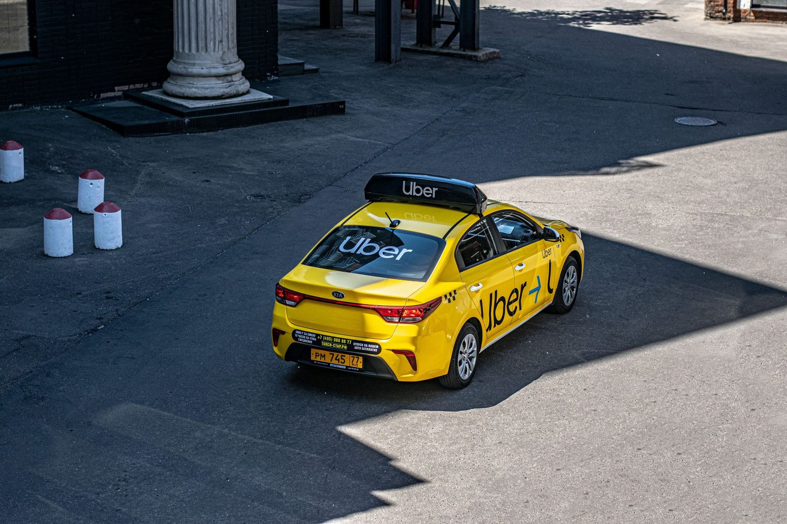 A yellow Uber taxi driving down a city street, photographed from above.
