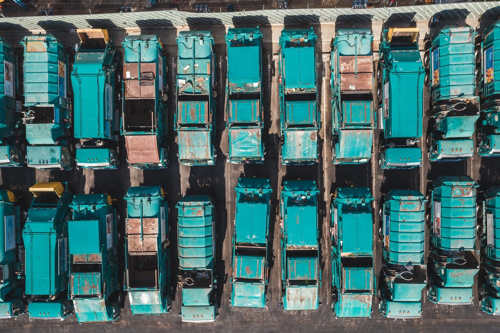 Aerial view of turquoise city garbage trucks parked in neat rows.