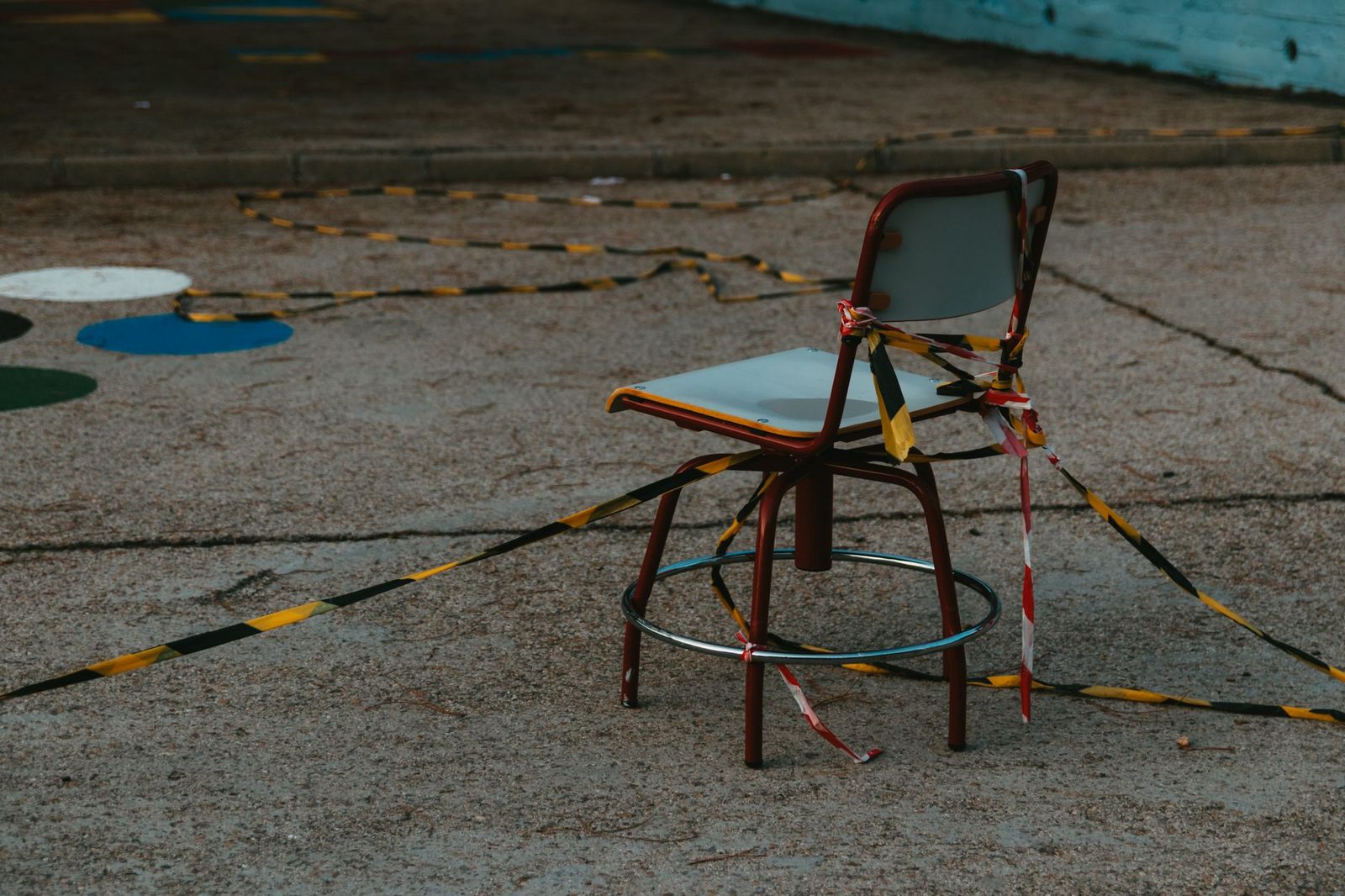 An empty metal chair wrapped in barricade tape sits on an outdoor paved surface.