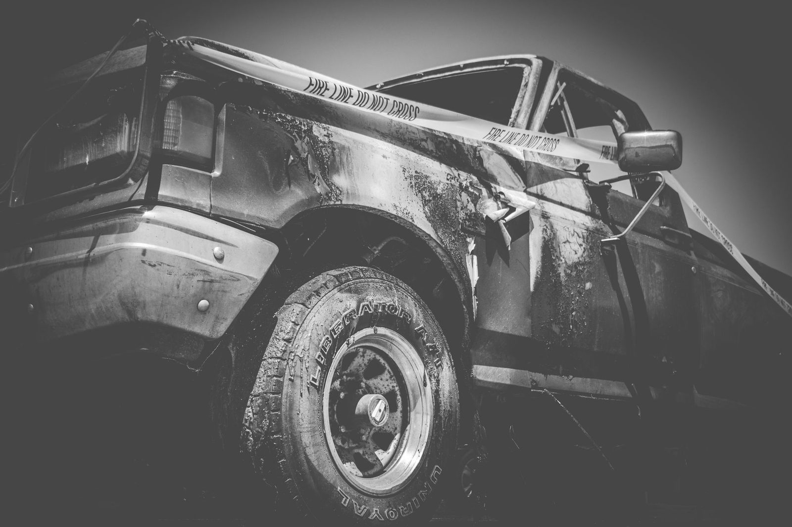 Black-and-white photo of a damaged truck behind police tape.