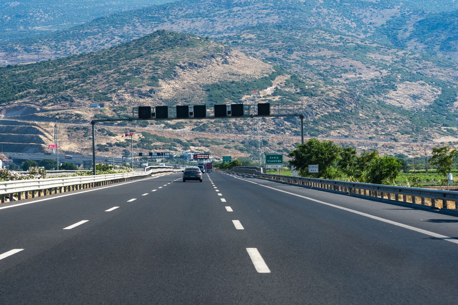 Cars travel along a long highway winding through rocky hills under a clear blue sky.