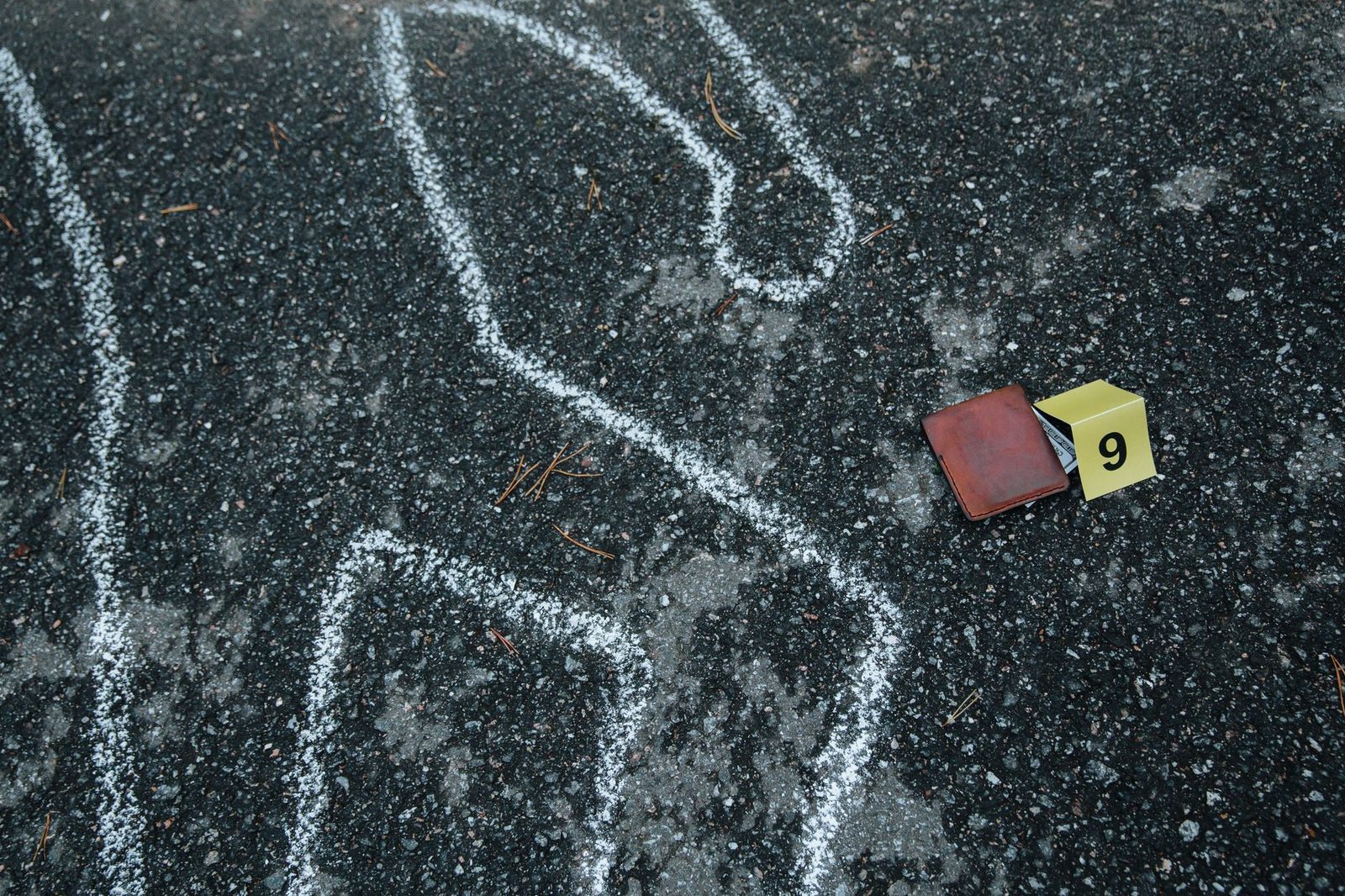 Chalk outline and evidence marker on an asphalt street surface.