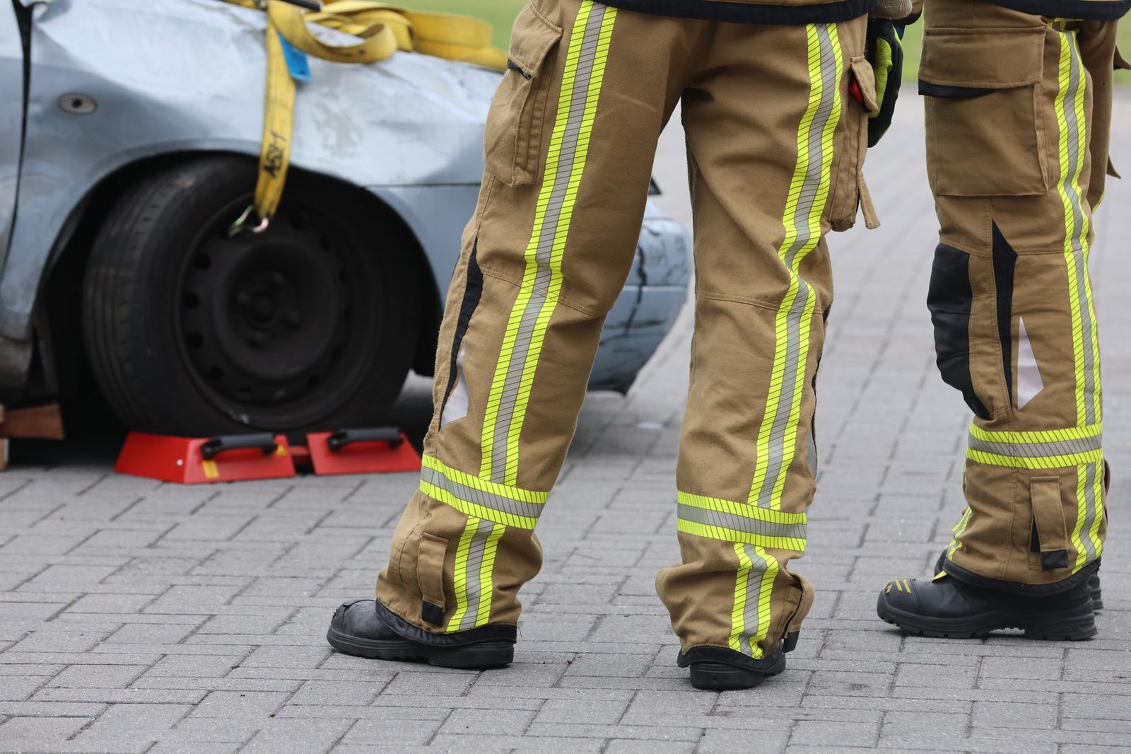 Firefighters in protective pants and boots inspect a damaged car after a road accident.