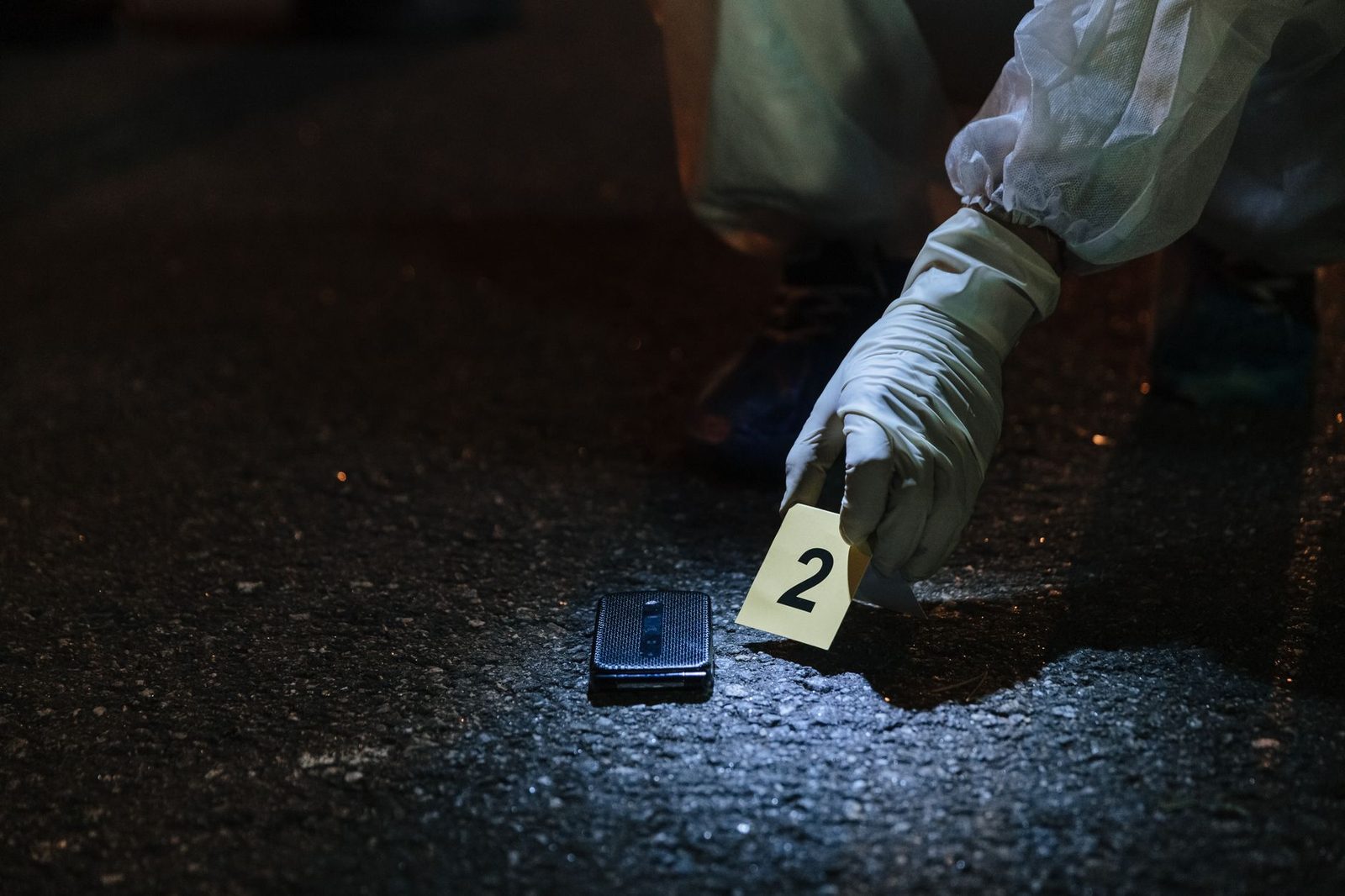 Forensic investigator examines evidence on a city street at night.