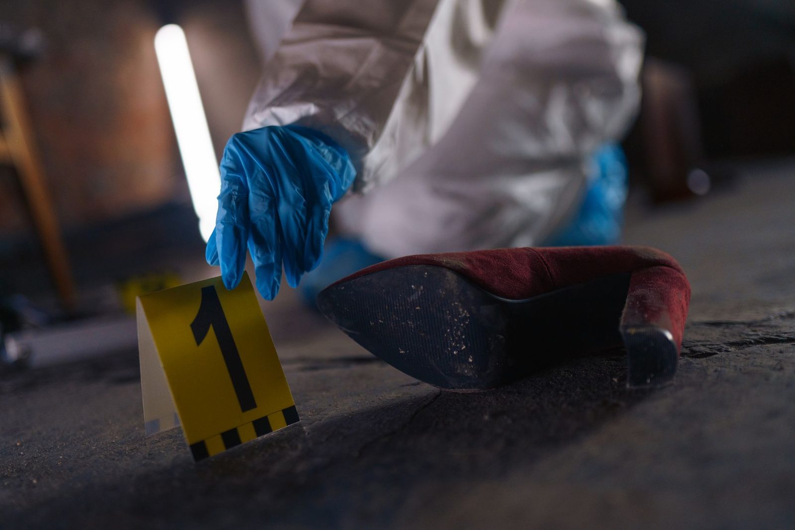 Gloved hand holding a shoe marked with a number-one evidence tag at a crime scene.