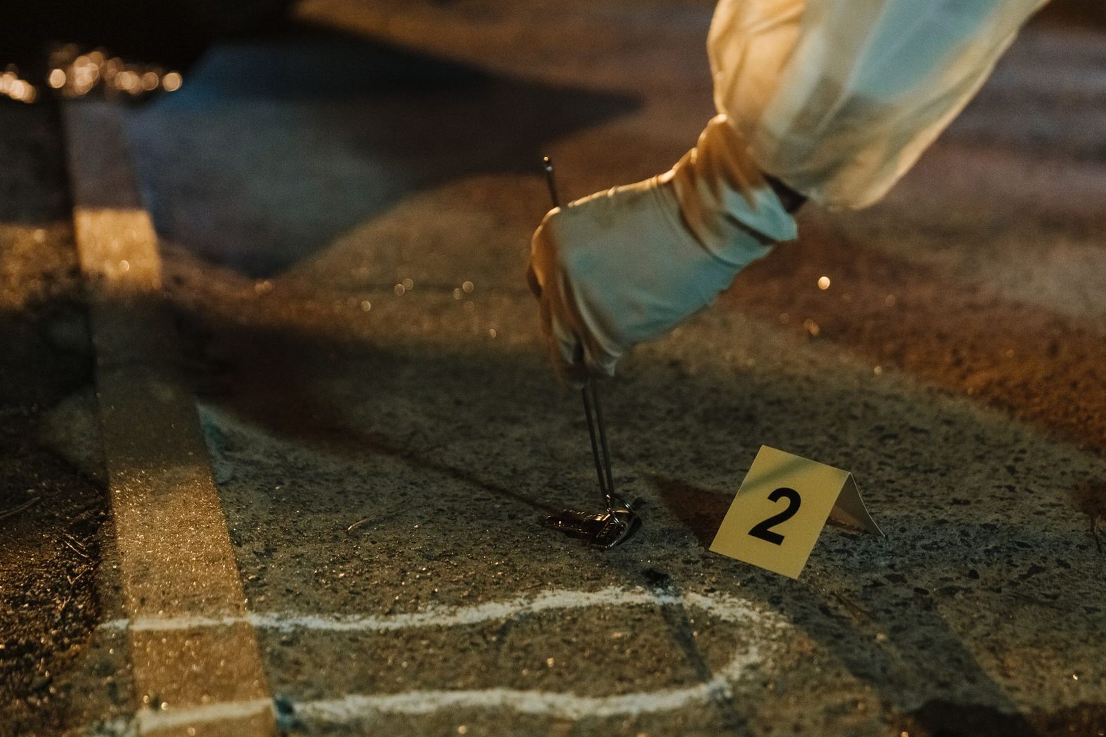 Gloved hands of a forensic investigator collecting evidence at a night crime scene