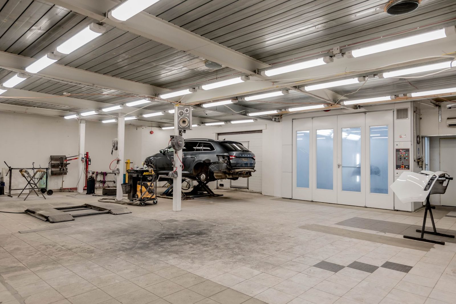 Interior of a modern auto repair garage with a car raised on a lift and tools nearby.