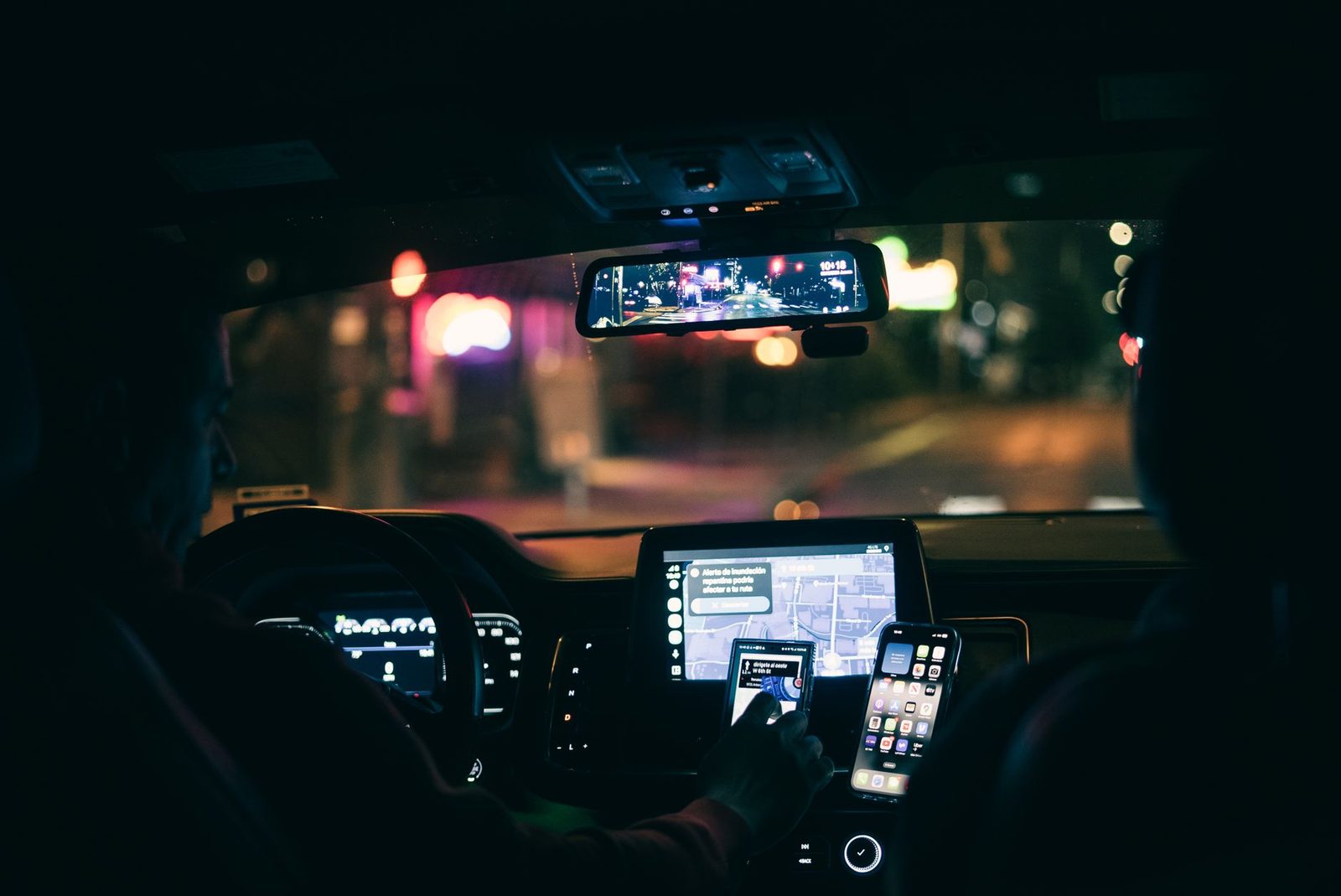 Interior view of a car at night as the driver checks a smartphone navigation app on a city street.