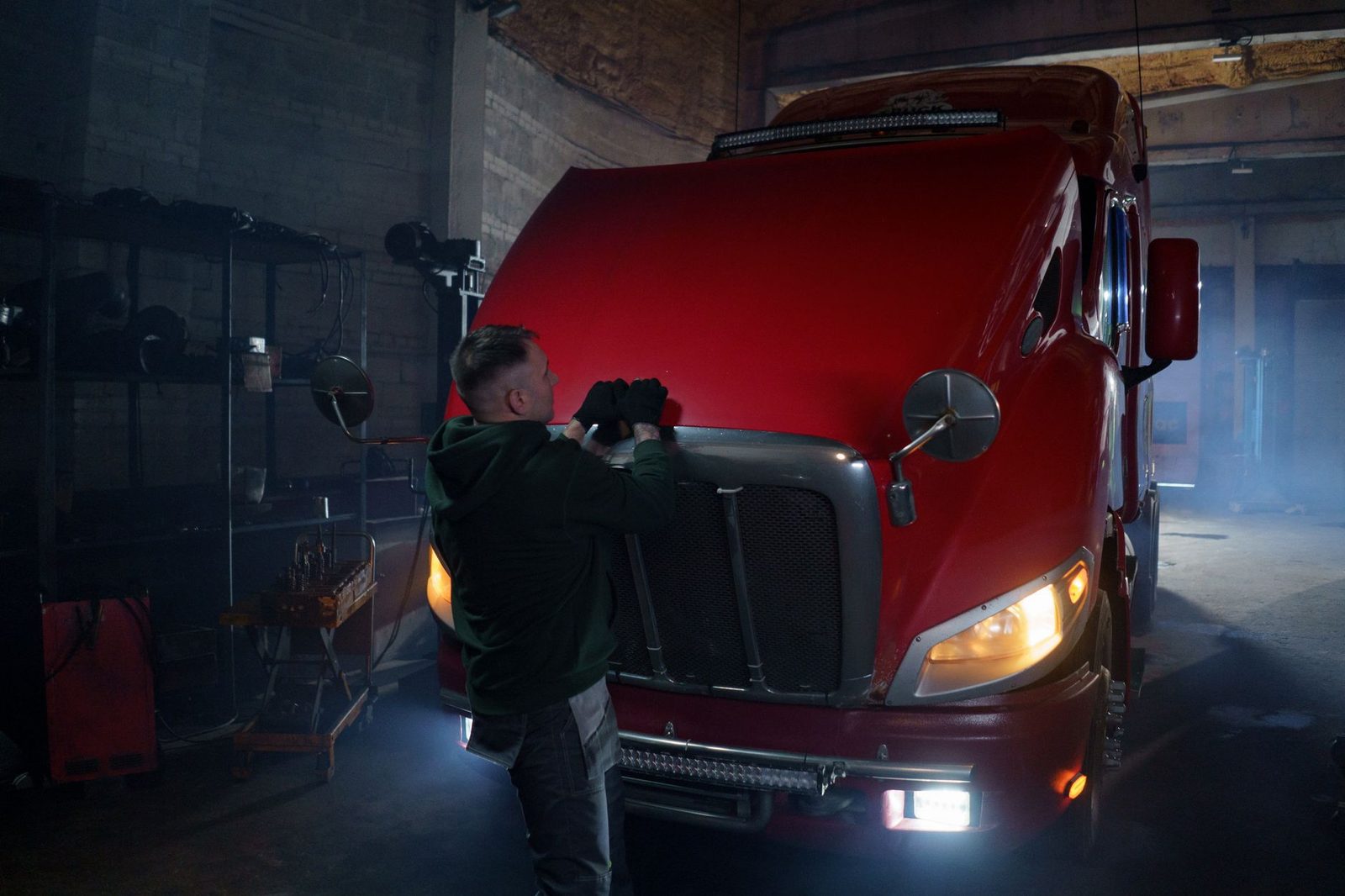 Mechanic in gloves working under the hood of a red truck in a dimly lit garage