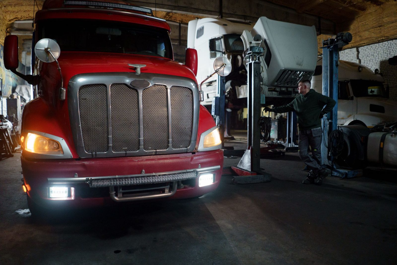 Red truck being serviced by a mechanic in a garage with vehicles raised on lifts