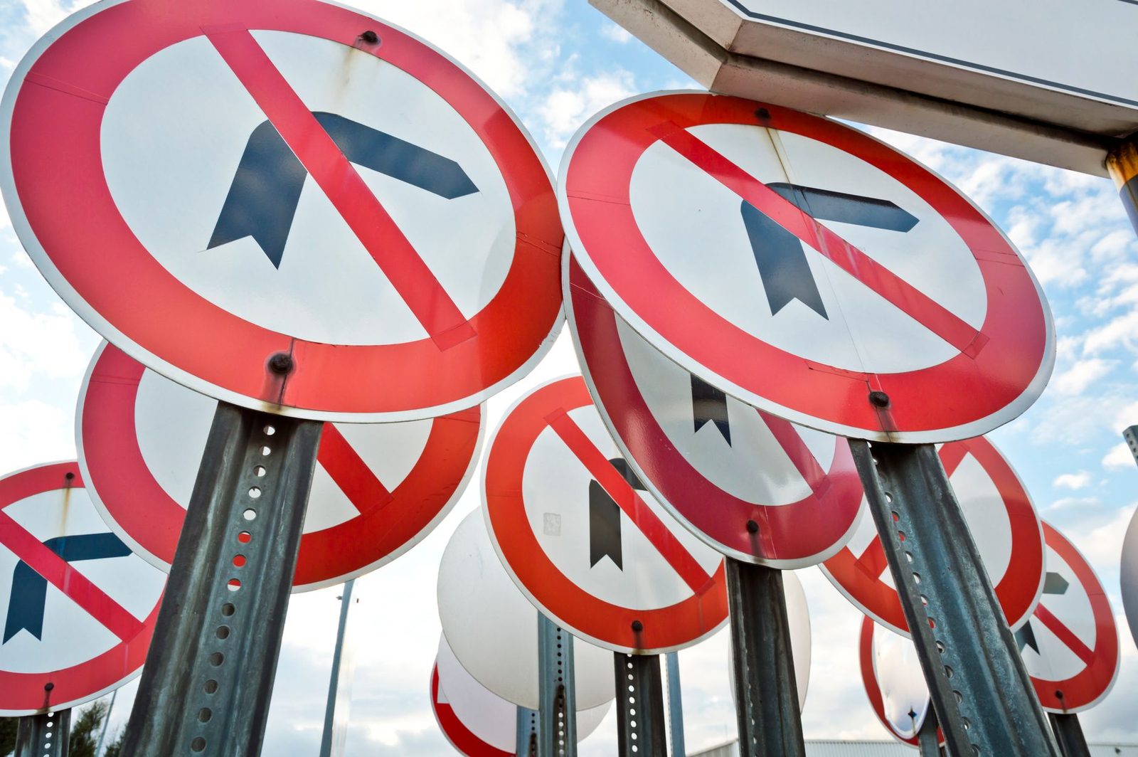 Several "No Left Turn" traffic signs mounted together against a blue sky.
