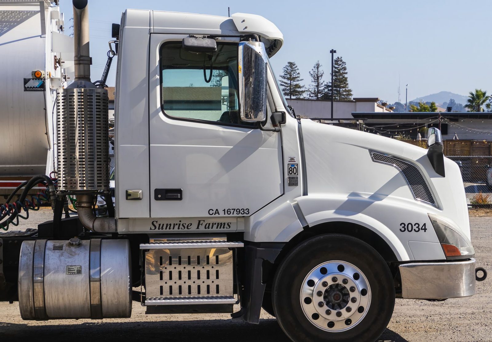 White semi-trailer truck parked in an outdoor industrial area, viewed from the side.